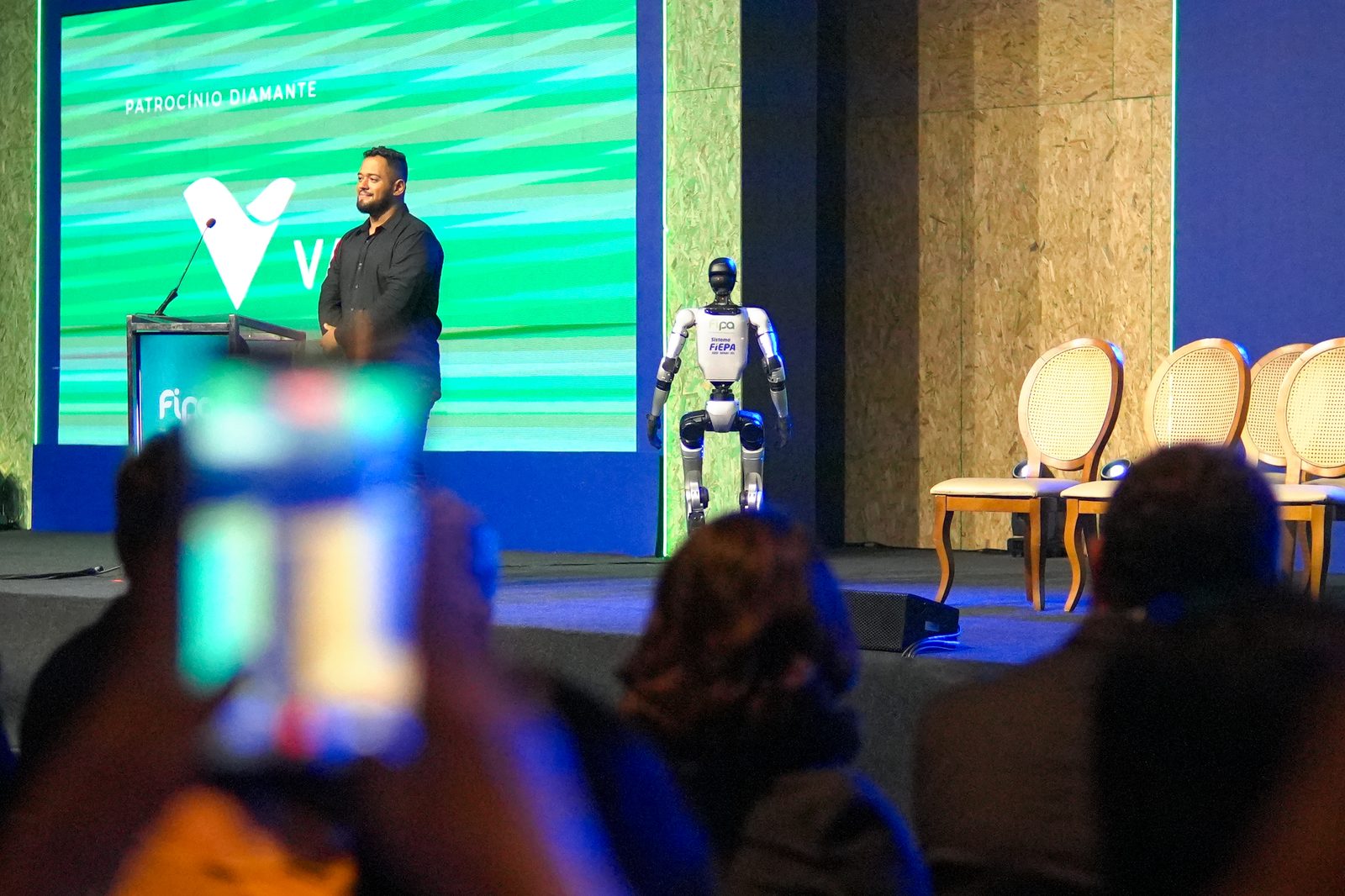 Palestrante no palco ao lado de robô humanoide